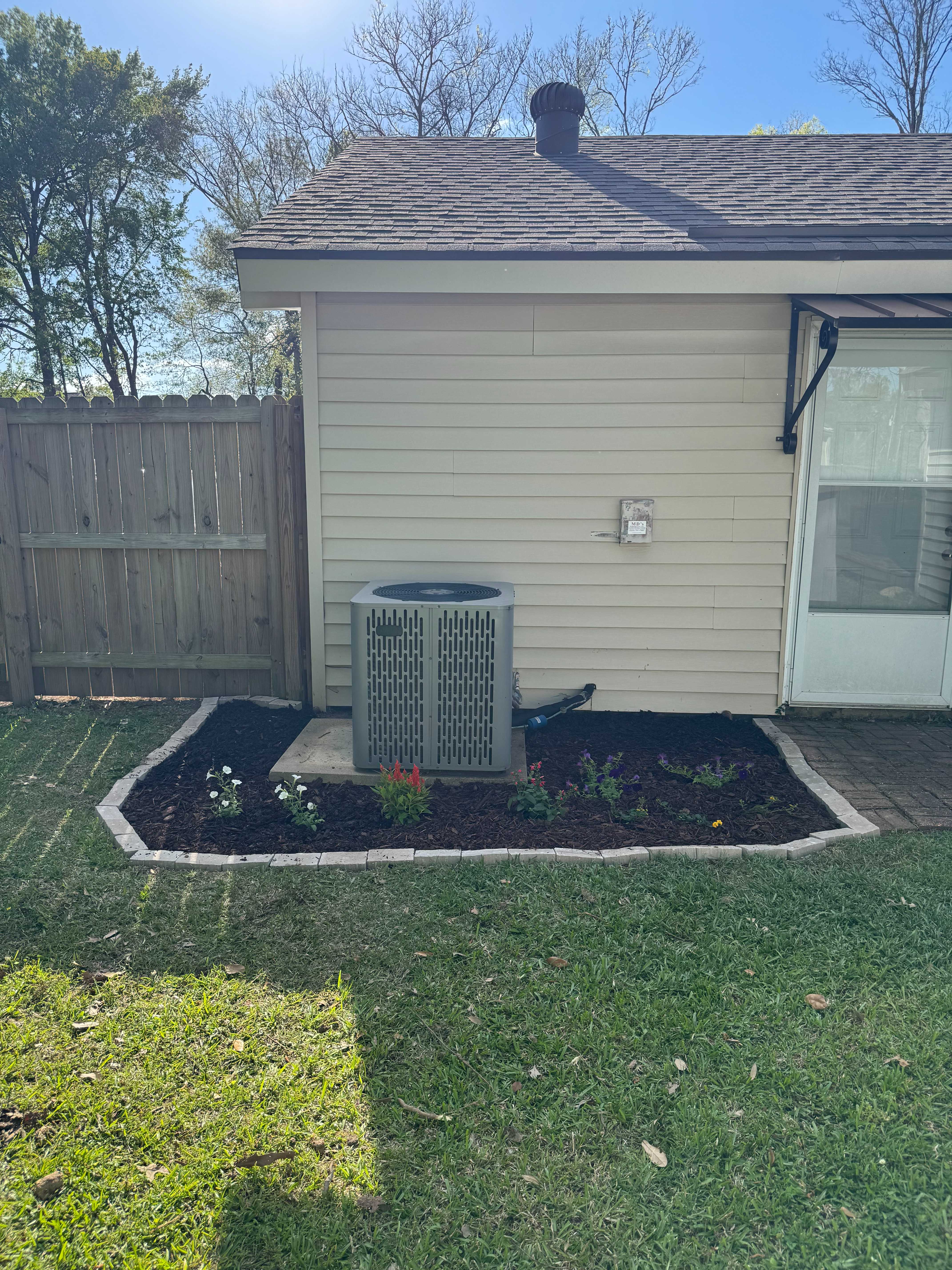 Newly installed mulch bed with fresh plants around an AC unit